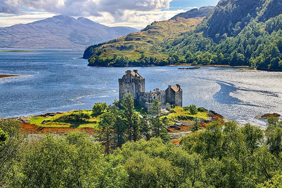 aerial photo of a Scottish castle on a river peninsula with lush green mountains in the background